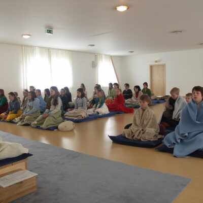 Kindern meditieren gemeinsam mit einem Assistenlehrer in der Meditationshalle